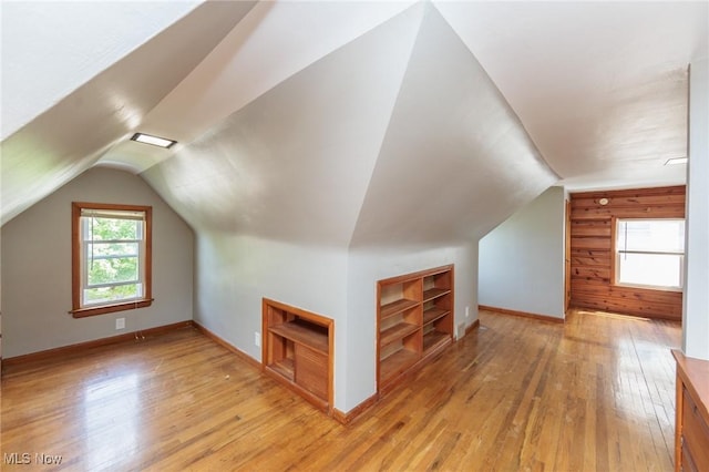 bonus room featuring built in features, light wood-type flooring, vaulted ceiling, baseboards, and wooden walls