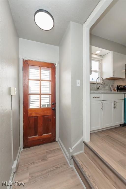 doorway with light wood-style flooring, a sink, and baseboards
