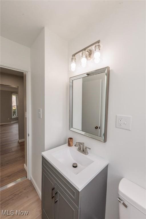 half bath featuring vanity, toilet, wood finished floors, and baseboards