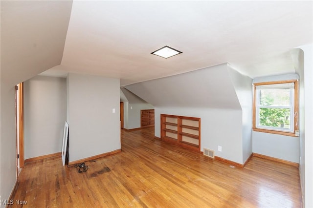 additional living space featuring light wood-style floors, lofted ceiling, and baseboards