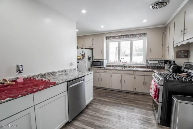 kitchen with appliances with stainless steel finishes, light stone counters, dark hardwood / wood-style flooring, ornamental molding, and sink