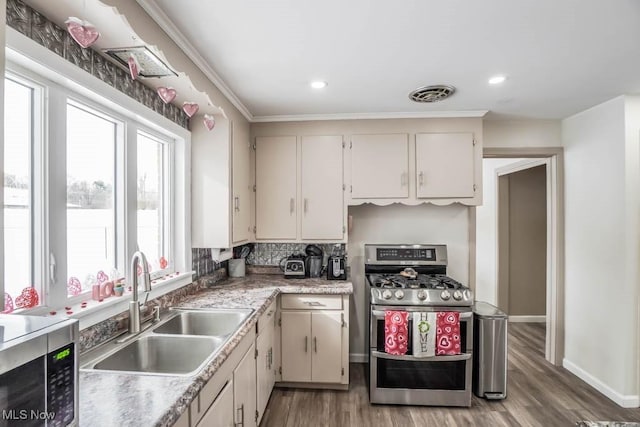 kitchen with stainless steel appliances, cream cabinetry, sink, backsplash, and hardwood / wood-style floors