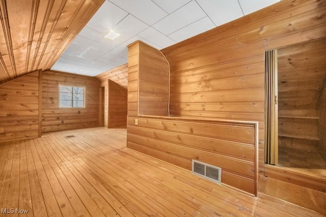 additional living space featuring lofted ceiling, visible vents, wood walls, and hardwood / wood-style flooring