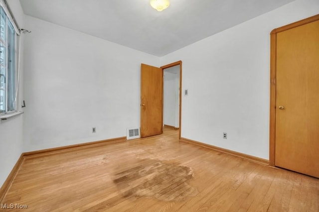 spare room featuring a healthy amount of sunlight, baseboards, visible vents, and hardwood / wood-style floors