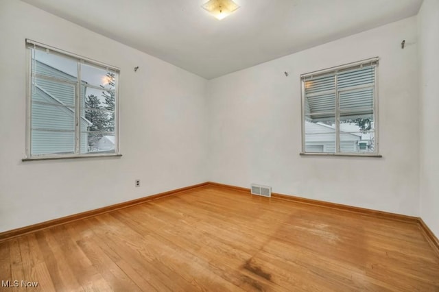 empty room with light wood finished floors, baseboards, visible vents, and a wealth of natural light