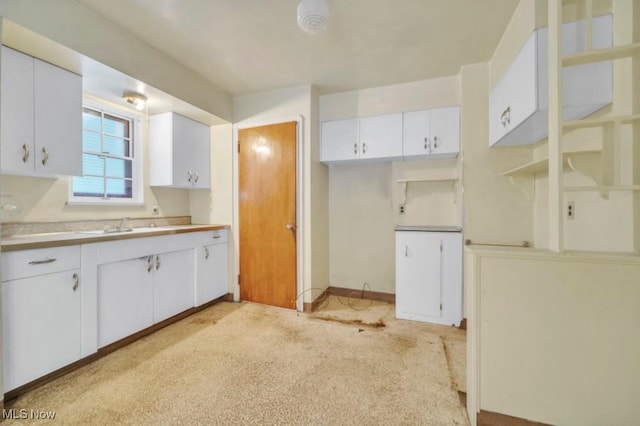 kitchen with light countertops, white cabinets, a sink, light carpet, and baseboards