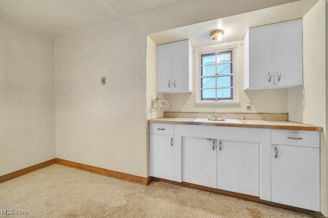 kitchen with white cabinetry, baseboards, light countertops, and a sink