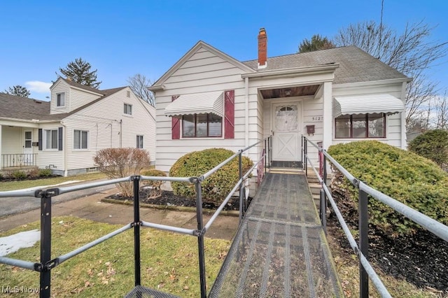 bungalow-style home with a chimney, fence, and roof with shingles