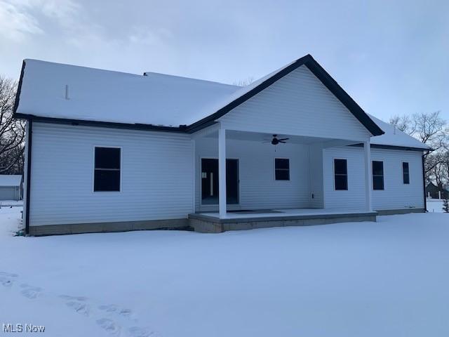 snow covered back of property with ceiling fan and a porch