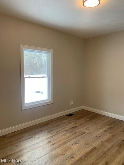unfurnished room featuring visible vents, baseboards, and wood finished floors