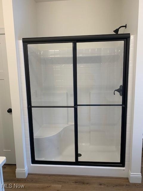 full bath featuring baseboards, a shower stall, and wood finished floors