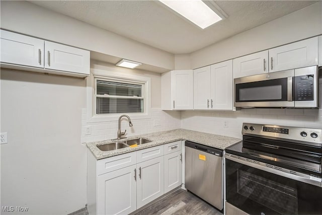 kitchen with appliances with stainless steel finishes, light stone countertops, white cabinets, backsplash, and sink