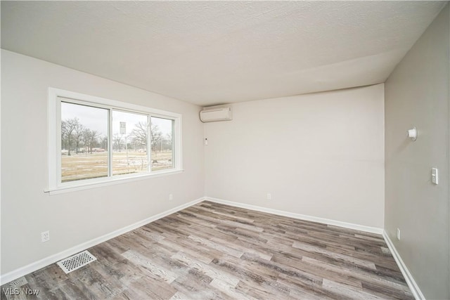 unfurnished room featuring an AC wall unit, light wood-type flooring, and a textured ceiling