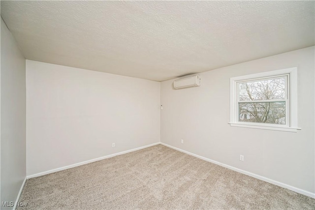 spare room featuring a wall mounted air conditioner, carpet flooring, and a textured ceiling