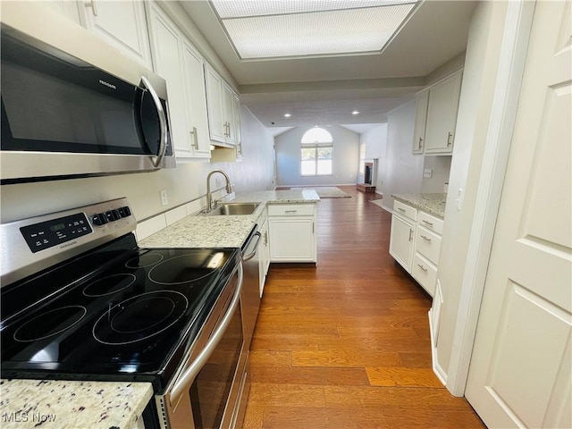 kitchen with appliances with stainless steel finishes, white cabinets, lofted ceiling, hardwood / wood-style floors, and sink