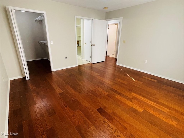 unfurnished bedroom featuring ensuite bath, a walk in closet, wood-type flooring, and a closet