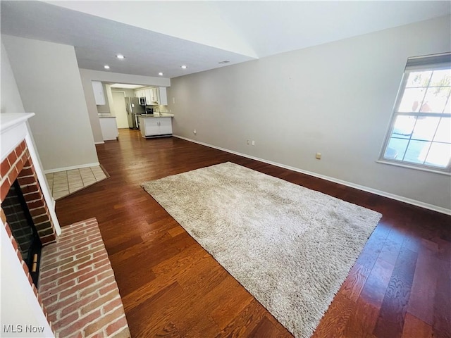 unfurnished living room featuring a brick fireplace and dark hardwood / wood-style floors