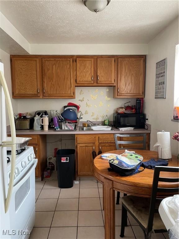 kitchen with light tile patterned flooring, dishwashing machine, white gas stove, and a textured ceiling