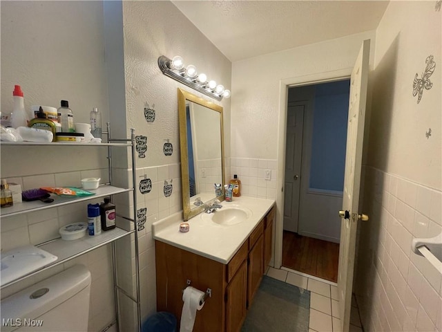 bathroom with tile walls, vanity, toilet, and tile patterned floors