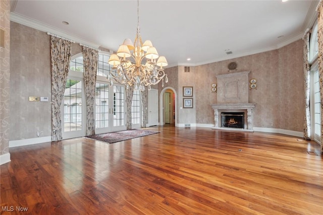 unfurnished living room with an inviting chandelier, french doors, wood-type flooring, and ornamental molding