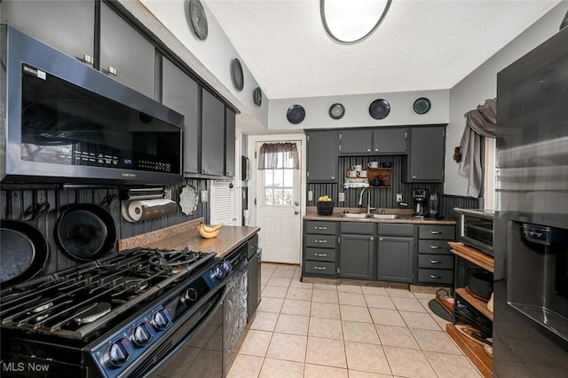 kitchen featuring appliances with stainless steel finishes, sink, light tile patterned flooring, gray cabinetry, and a textured ceiling