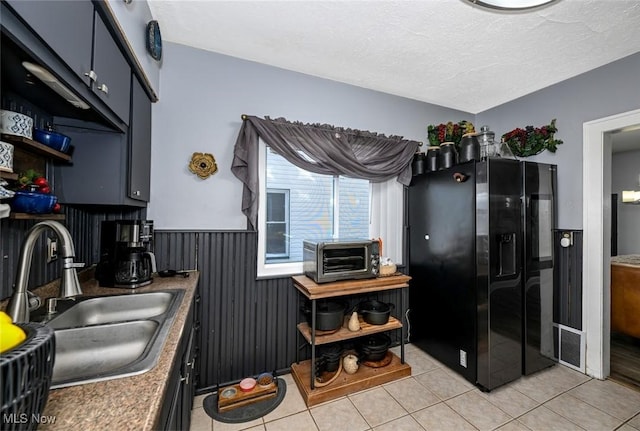 kitchen featuring light tile patterned floors, sink, black fridge, and a textured ceiling