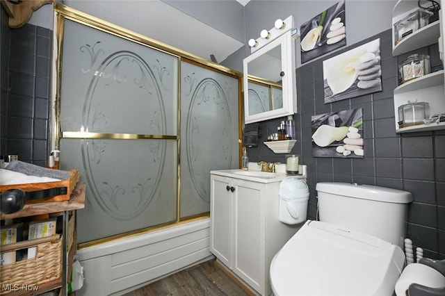 full bathroom featuring wood-type flooring, tile walls, vanity, combined bath / shower with glass door, and toilet