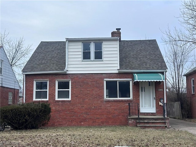 view of front facade featuring roof with shingles, a chimney, a front lawn, and brick siding