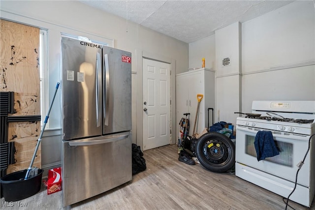 kitchen featuring stainless steel refrigerator, white gas range, a textured ceiling, and light hardwood / wood-style flooring