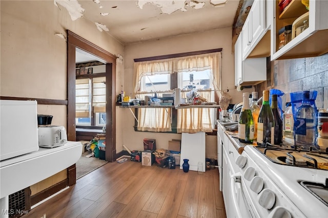 kitchen with tasteful backsplash, white gas range oven, glass insert cabinets, wood finished floors, and white cabinetry