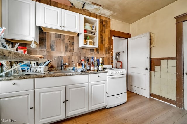 kitchen with light wood finished floors, white cabinetry, white range with gas cooktop, a sink, and dark stone counters