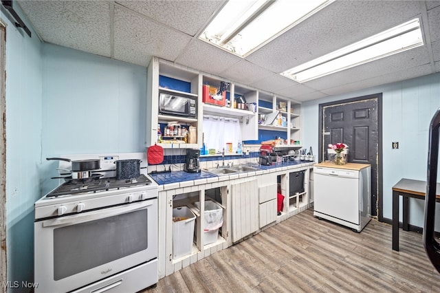 kitchen with white appliances, light wood-type flooring, white cabinets, tile counters, and sink