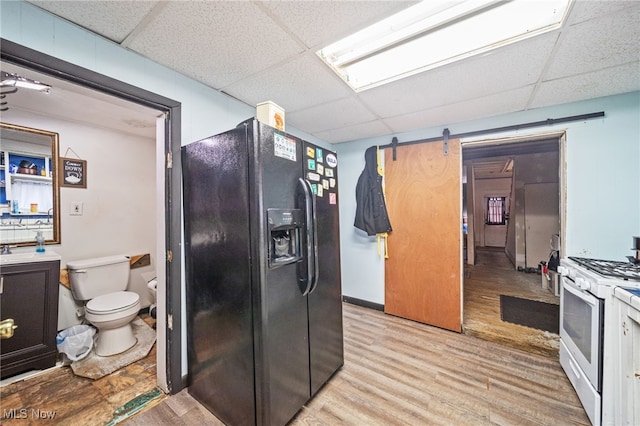 kitchen featuring light hardwood / wood-style flooring, a barn door, black refrigerator with ice dispenser, a paneled ceiling, and white range with gas stovetop