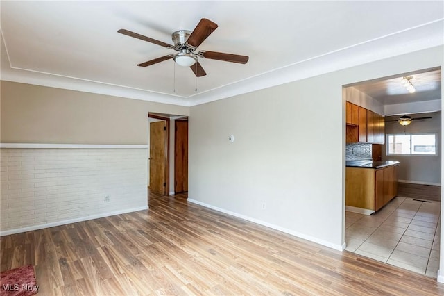 unfurnished living room featuring light hardwood / wood-style flooring, ceiling fan, and brick wall