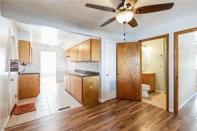 kitchen with a textured ceiling, ceiling fan, decorative backsplash, and light hardwood / wood-style flooring