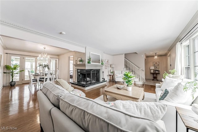 living room with hardwood / wood-style flooring, a notable chandelier, french doors, a fireplace, and ornamental molding