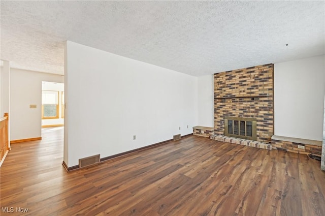 unfurnished living room with a brick fireplace, visible vents, a textured ceiling, and wood finished floors