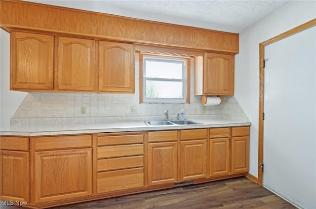 kitchen featuring tasteful backsplash, dark wood-type flooring, light countertops, a textured ceiling, and a sink