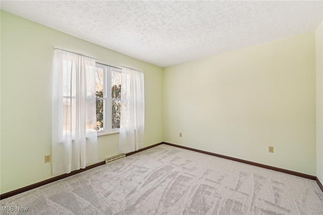 spare room featuring light carpet, baseboards, visible vents, and a textured ceiling