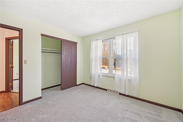 unfurnished bedroom with light colored carpet, visible vents, a textured ceiling, and baseboards