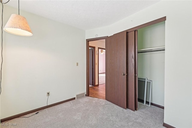 unfurnished bedroom featuring a closet, visible vents, light carpet, a textured ceiling, and baseboards