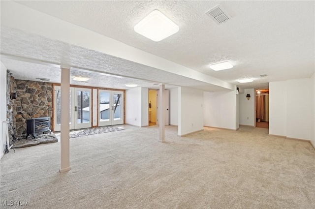 basement with a wood stove, light carpet, visible vents, and a textured ceiling