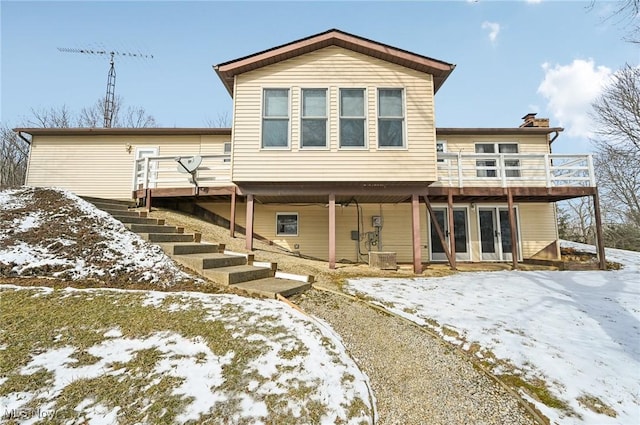 snow covered back of property featuring stairs, a chimney, a wooden deck, and central air condition unit