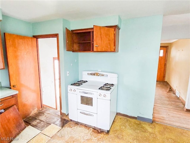 kitchen featuring visible vents, white gas stove, brown cabinets, open shelves, and light countertops