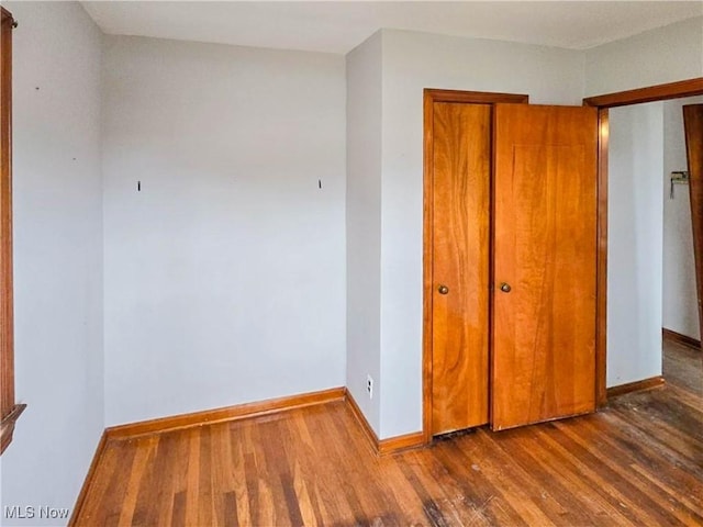 unfurnished bedroom featuring baseboards, wood finished floors, and a closet