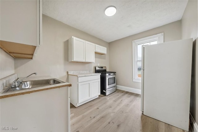 kitchen with stainless steel stove, sink, white refrigerator, and white cabinets