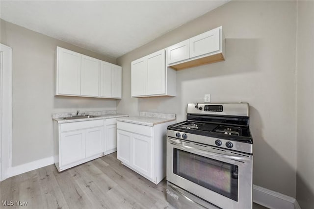 kitchen featuring white cabinets, sink, stainless steel gas range, and light wood-type flooring