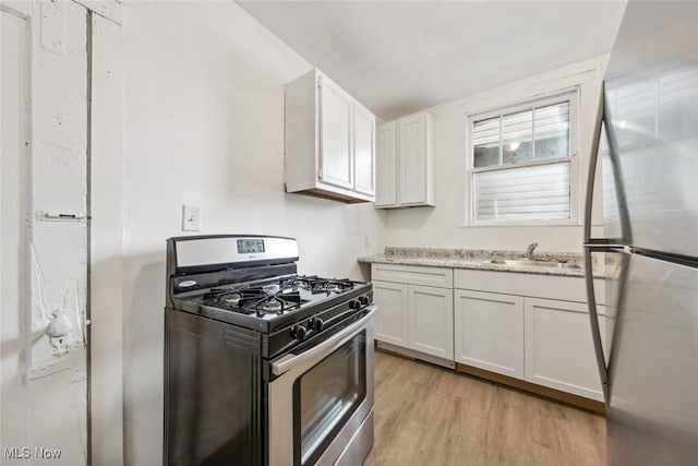 kitchen featuring appliances with stainless steel finishes, light wood-type flooring, light stone countertops, sink, and white cabinetry