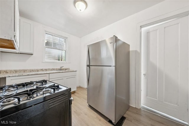 kitchen featuring sink, white cabinets, stainless steel fridge, and black gas stove