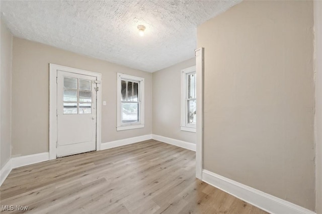 unfurnished room with light wood-type flooring and a textured ceiling